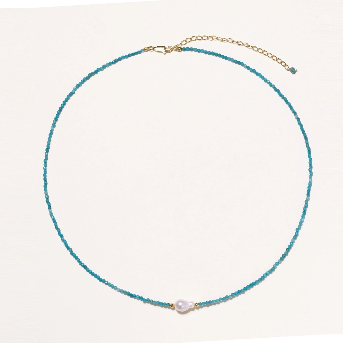 Delicate gold vermeil necklace with teal apatite beads and freshwater pearl on white background.